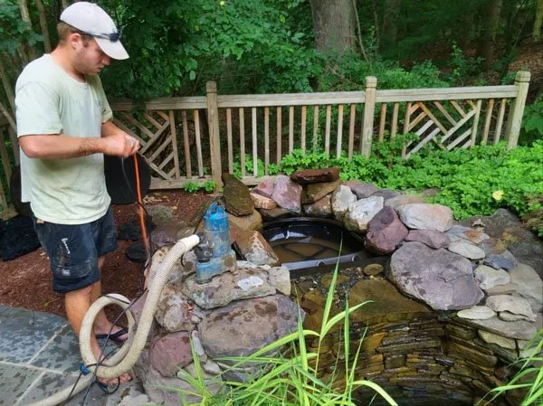 a man is using a hose to clean a pond.