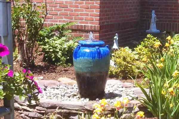 a blue and green water fountain surrounded by flowers.