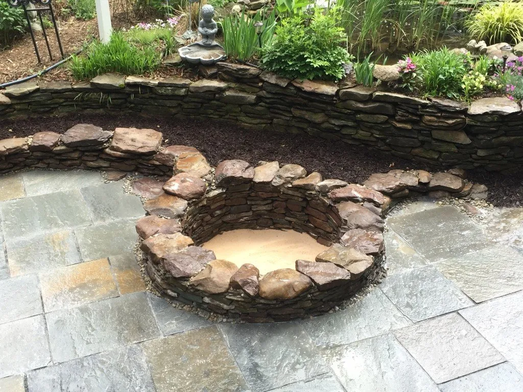 a stone fire pit surrounded by a garden.