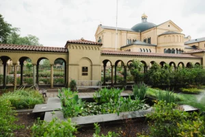 Courtyard garden with rectangular ponds and lush plants, an arched colonnade, and a domed beige building in the background.